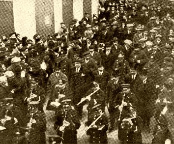 Paso por el domicilio de Raimundo Sarriegui de la Banda Municipal seguida de un nutrido número de autoridades municipales y representantes de las sociedades donostiarras en el momento del descubrimiento de la lápida conmemorativa
